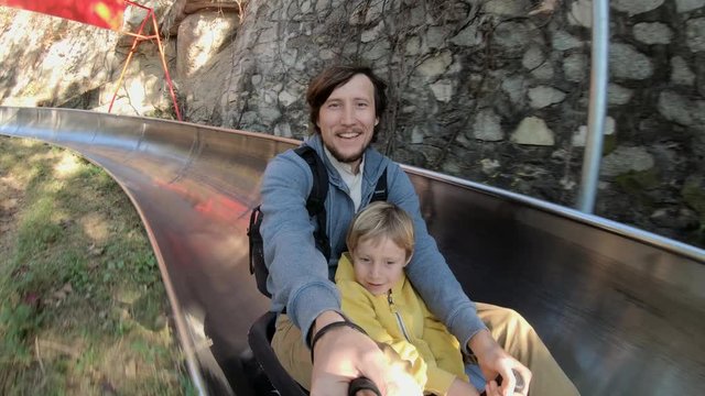 Slowmotion shot of a father and son riding down the alpine roller coaster in an autumn forest