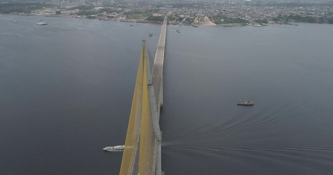 High aerial above the cable-stayed Rio Negro Bridge that links the cities of Manaus and Iranduba in the Brazilian Amazon as a boat passes underneath the bridge followed by its wake and traffic crosses
