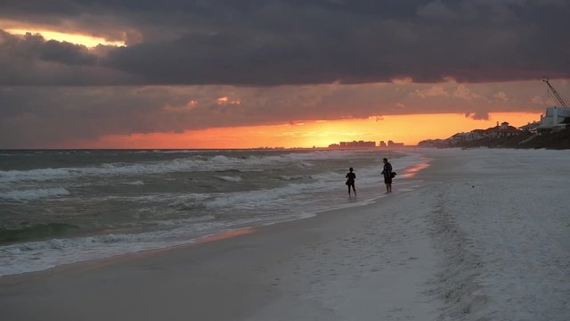 Couple people silhouette watching dramatic orange red sunset in Santa Rosa Beach, Florida with Pensacola coastline coast in panhandle with ocean gulf mexico waves