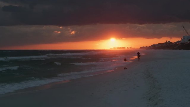 Couple people dark silhouette watching dramatic orange red sunset in Santa Rosa Beach, Florida with Pensacola coastline coast in panhandle with ocean gulf mexico waves