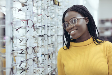 Young pretty african woman choosing prescription glasses frames in Optician's shop.