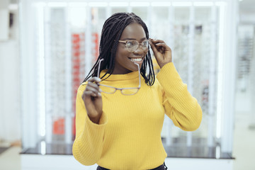 Young pretty african woman choosing between two eyeglasses frames in Optician shop