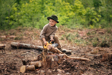 The boy, 5 years old, looks like a trapper, wanderer, lumberjack. Hut, shelter in the forest among logs of wood. A lonely walk, rest after work. Survival.