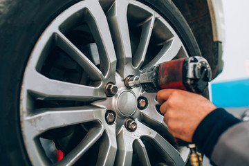 Obraz premium Mechanician changing car wheel in auto repair shop. Mechanic adjusting the tire wheel by using hand and tool at the repair car garage