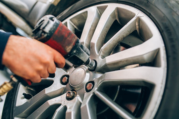 Mechanician changing car wheel in auto repair shop. Mechanic adjusting the tire wheel by using hand...