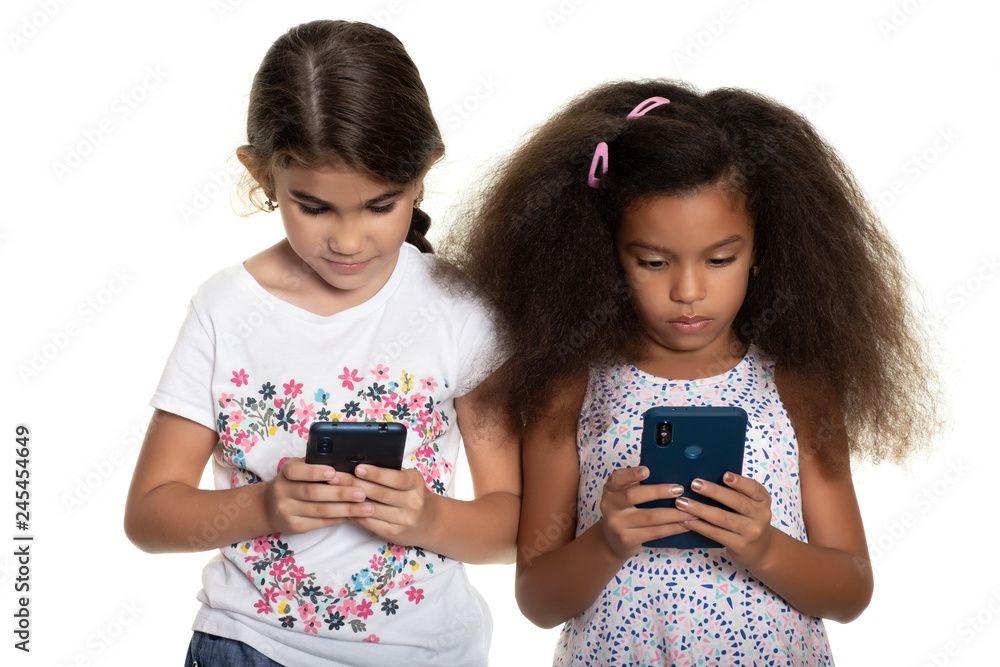 Wall mural two small girls using their smartphones on a white background