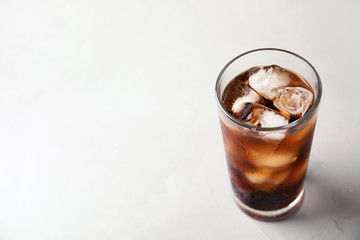 Glass of refreshing cola with ice on light table. Space for text