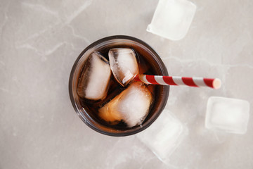 Glass of cola with ice on grey background, top view