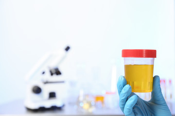 Laboratory assistant holding urine sample in container indoors, closeup with space for text....