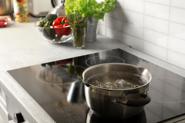 Pot with boiling water on electric stove in kitchen, space for text