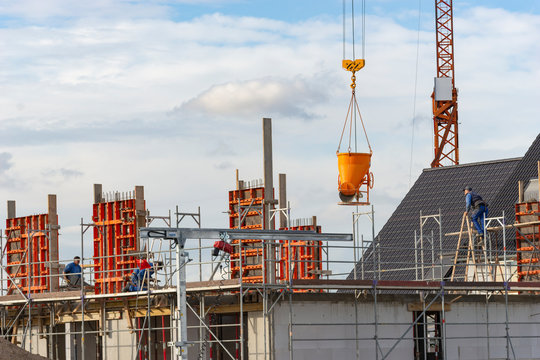 Baustelle mit Bauarbeitern und Kran an dem ein Betonk&uuml;bel h&auml;ngt.
