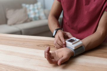 Man checking blood pressure at table indoors, closeup with space for text. Cardiology concept