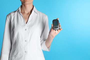 Female doctor holding digital glucometer on color background, closeup view with space for text. Medical object