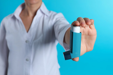 Female doctor holding asthma inhaler on color background, closeup. Medical object