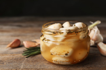 Preserved garlic in glass jar on wooden table, closeup. Space for text