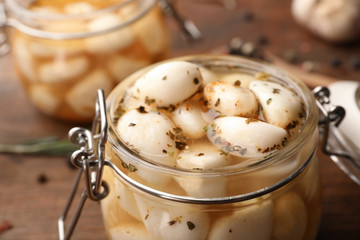 Fototapeta na wymiar Preserved garlic in glass jar on wooden table, closeup