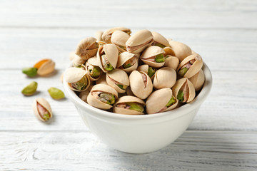 Organic pistachio nuts in bowl on wooden table, closeup
