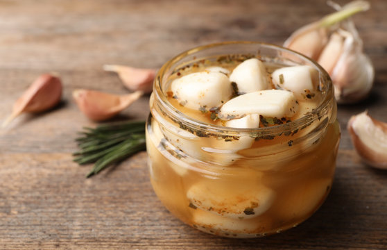 Preserved garlic in glass jar on wooden table, closeup