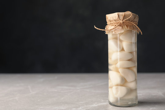 Preserved garlic in glass jar on table. Space for text
