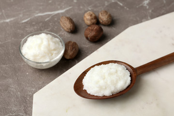 Fototapeta na wymiar Shea butter in wooden spoon and bowl with nuts on grey background