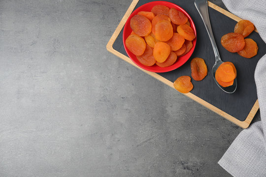 Plate and spoon of dried apricots on grey background, top view with space for text. Healthy fruit