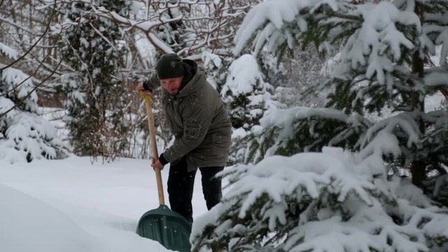 A young man cleans the snow in his yard. Bearded man cleans snow near his house.
