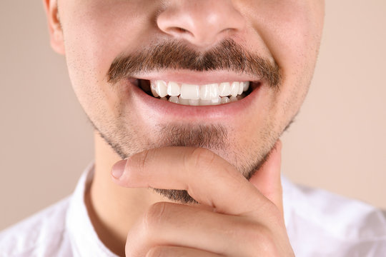 Young man with healthy teeth smiling on color background, closeup
