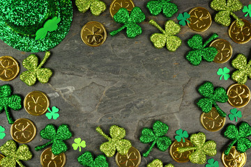 St Patricks Day frame with shamrocks, gold coins and leprechaun hat over a dark slate background