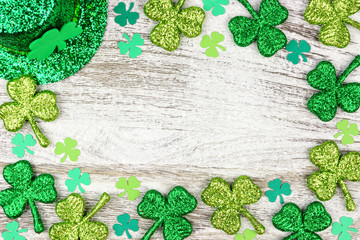 St Patricks Day frame border of shamrocks with leprechaun hat over a rustic white wood background