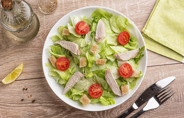Caesar salad with chicken on a light natural table with cutlery.
