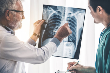 Senior male doctor looking at x ray film of patient chest injury while working with another doctor at the hospital. Medical healthcare staff and doctor service.