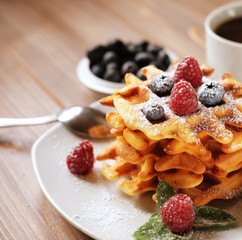 Waffles with  berries on a white plate and coffee, close up.