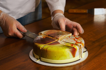 Confectioner cuts dacquoise cake in mirrored glaze. Modern cooking. Woman holds on knife piece of cake. Seen cakes and stuffing. Yummy