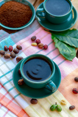 Cup with black coffee served outside with raw green, mature red and roasted coffee beans, decorated with green leaves from coffee plant