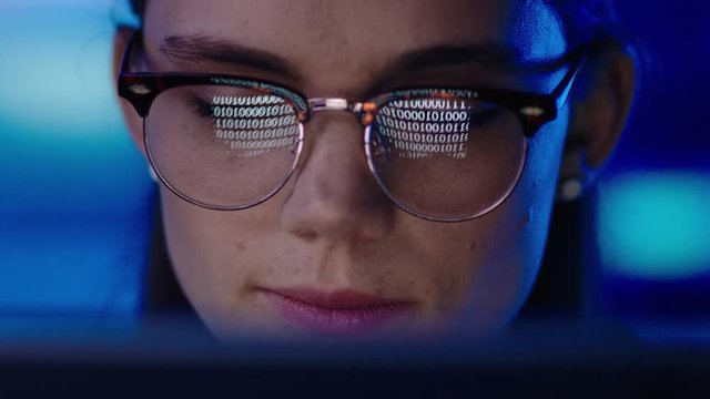 close up portrait young woman programmer using computer browsing code data looking at binary information on screen wearing glasses