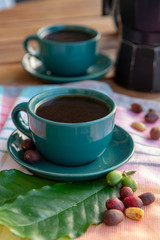 Cup with black coffee served outside with raw green, mature red and roasted coffee beans, decorated with green leaves from coffee plant