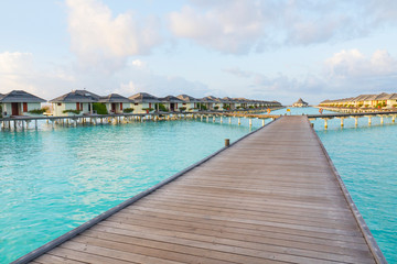 Obraz premium Water Bungalows at Tropical beach in the Maldives at summer day. Sea and the resort like paradise relax concept. Long wodden jetty extended into azure water of lagoon with villas over the ocean.