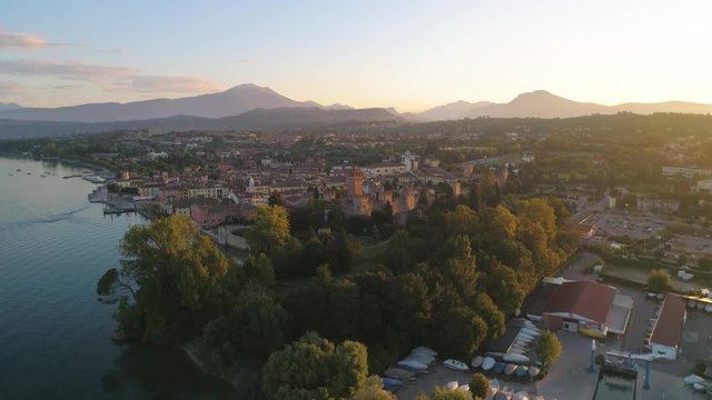 Italian castle, C4k aerial, reverse, drone shot, of Lazise fortress, at lago di Garda, on a sunny, summer morning dawn, in Verona, Italy