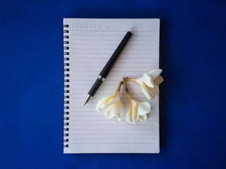 Pencil and flowers on a notebook on a blue background