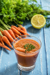 Fresh carrot smoothie in glass on rustic wooden background.