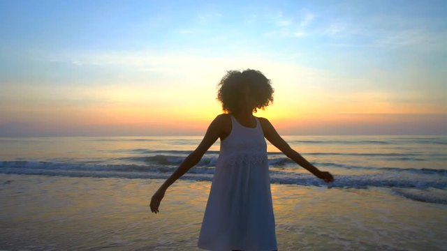 Silhouette of slim African American female dancing on sea coast at sunset