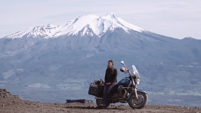 Hispanic woman resting on the motorcycle, snowed volcano on the background. Slow motion