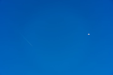 An airplane flying in the sky and half moon appear.