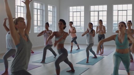 yoga class of healthy women practicing warrior pose enjoying exercising in fitness studio instructor leading group meditation teaching workout posture at sunrise