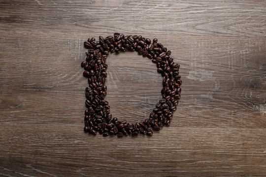 Fototapeta Dark roasted coffee bean arranged on a wooden table in the shape of text alphabet letter D