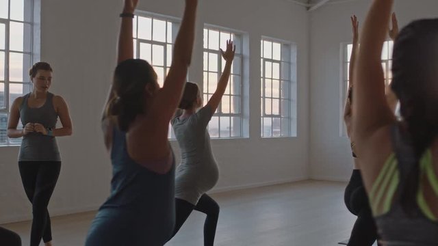 yoga class instructor teaching healthy pregnant women practicing warrior pose enjoying group training exercise in fitness studio at sunrise