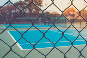 Fototapeta premium Close up metal fence with empty outdoor blue tennis hard court in the background. (Selective focus)