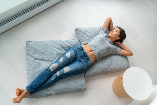 Home lifestyle happy Asian woman relax lying down on living room floor pillows relaxing contemplative looking at windows. New condo apartment satisfaction homeowner young girl enjoying house.