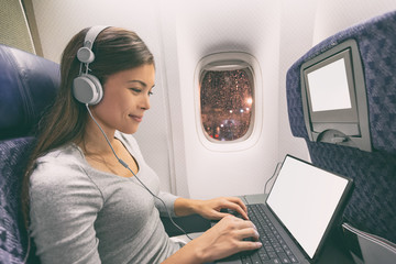 Fototapeta premium Samolot pasażerski biznes kobieta profesjonalna praca w kabinie samolotu podczas lotu z wifi w czasie pisania pisania na komputerze typu tablet słuchanie muzyki w słuchawkach. Młody podróżnik azjatycki.