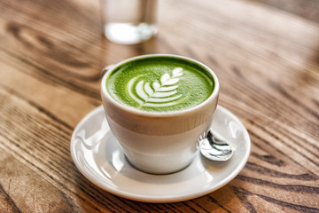 Matcha latte green milk foam cup on wood table at cafe. Trendy powered tea trend from Japan. - obrazy, fototapety, plakaty